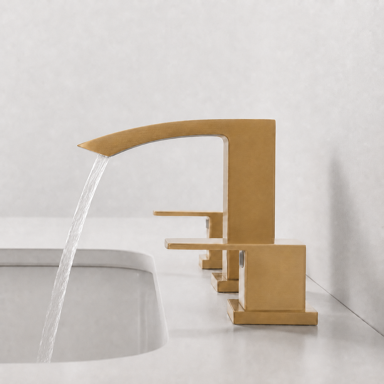 A modern single-handle faucet in a brushed gold finish, shown with water flowing from the spout into a white sink against a light gray wall.