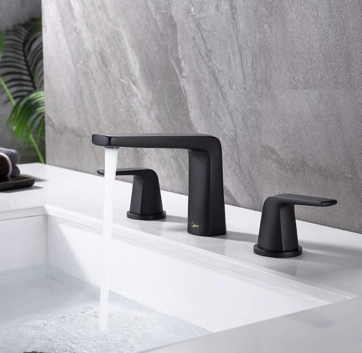 Two handle widespread bathroom faucet in matte black finish, installed in a bathroom setting with a plant in the background.