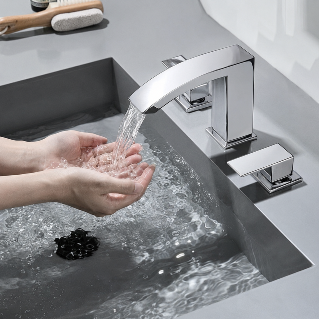 A modern chrome three-hole bathroom faucet with a single lever handle, shown installed in a sink with water running from the spout. A person's hands are visible under the stream, and a soap dish is in the background.