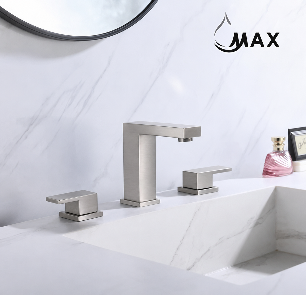 A modern three-hole bathroom faucet set with two separate handles in a brushed silver finish, installed on a white marble sink against a matching marble backsplash. A black circular mirror is partially visible at the top, and a pink perfume bottle and a small picture frame sit on the right side of the counter.