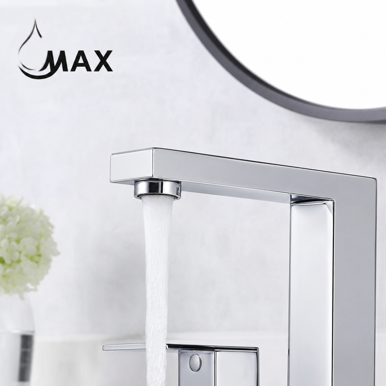 A modern chrome single-handle faucet with water running from the spout, shown against a light bathroom wall with a round mirror and a small white flower arrangement in the background. The brand name MAX is visible in the upper left.