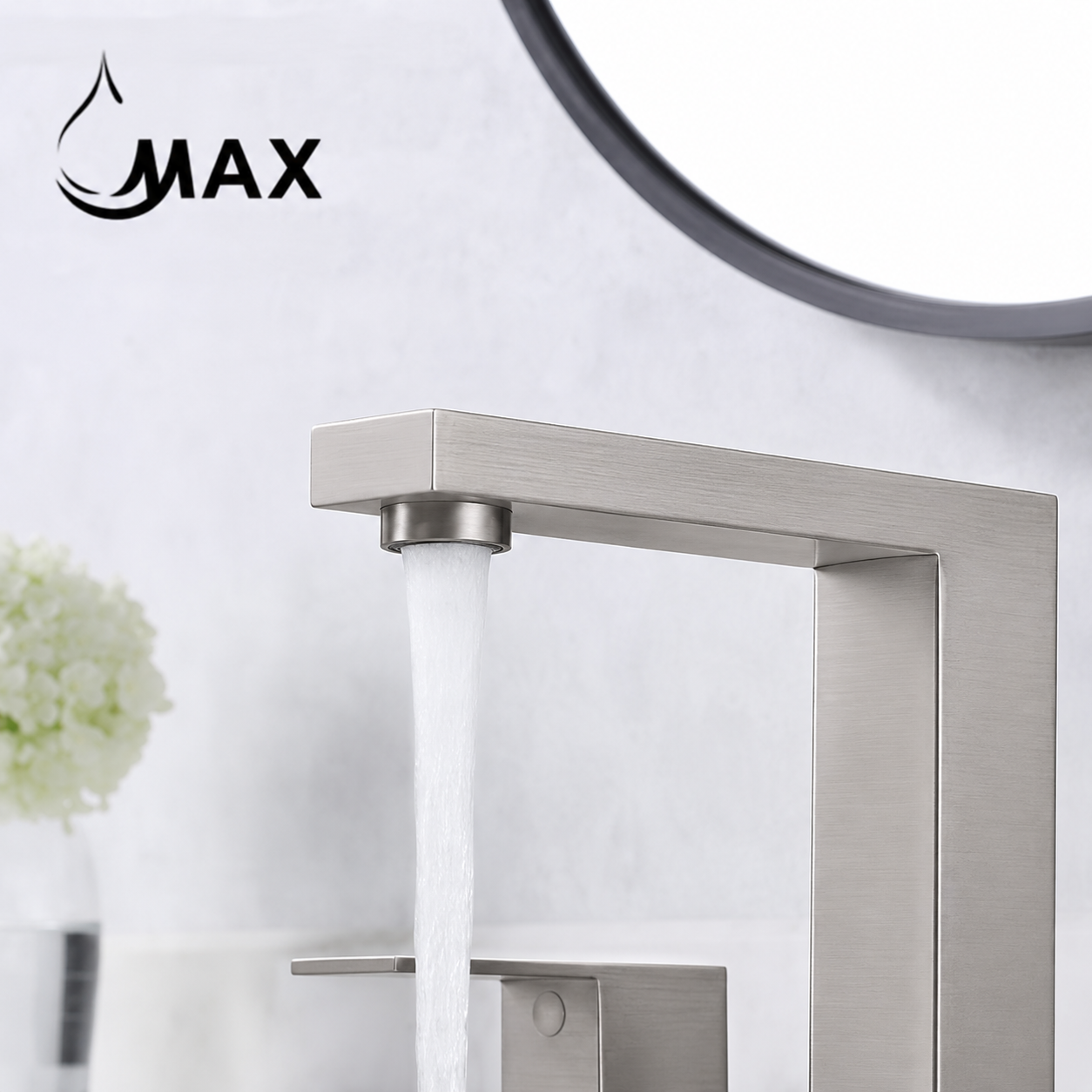 A modern rectangular wall-mounted faucet in brushed stainless steel with water flowing from the spout, shown against a light bathroom wall with a round mirror edge and a small floral decor element.