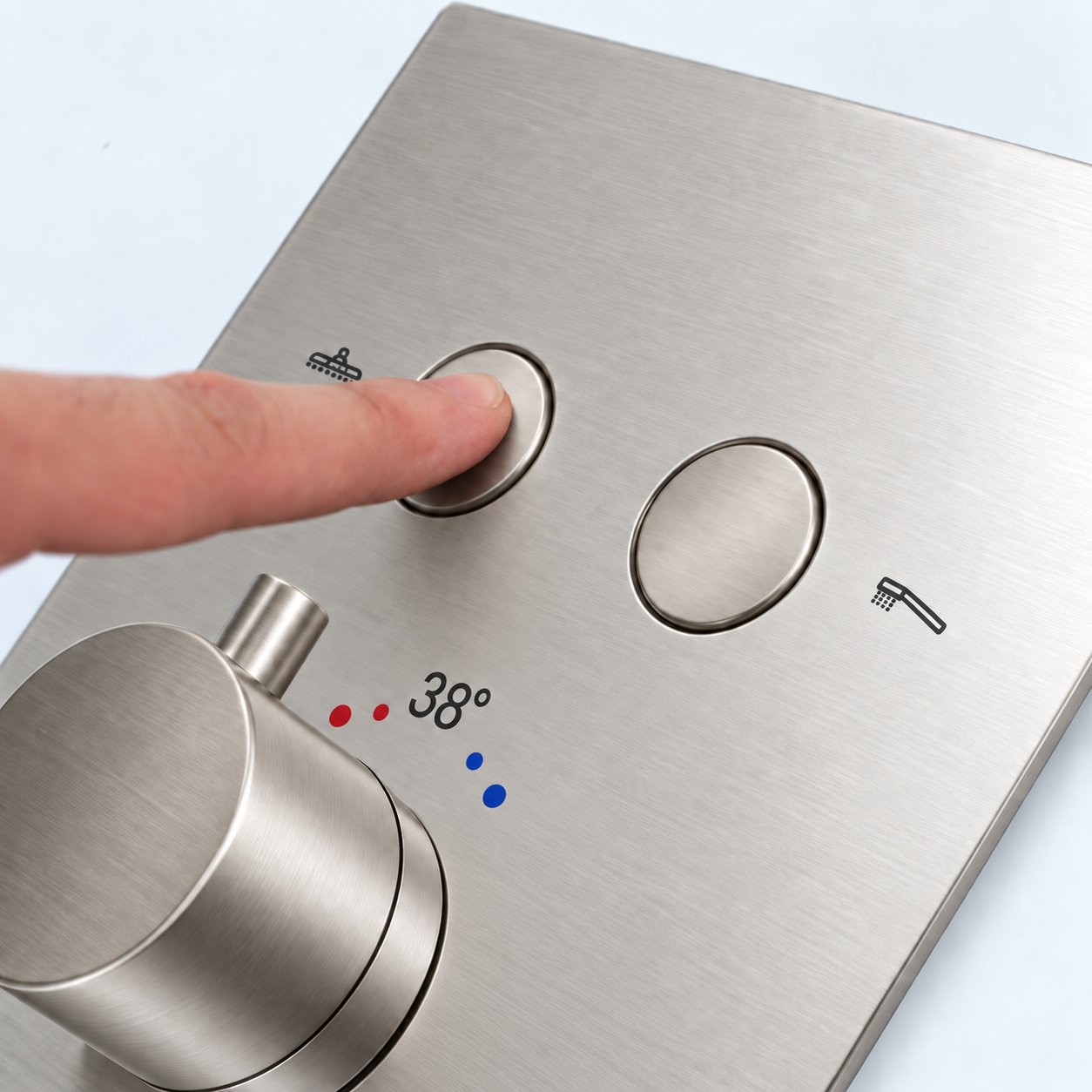 Close-up of a brushed metal thermostatic shower valve control panel with a finger pressing a button, showing the shower head icon, temperature dial, and 38 degrees setting.