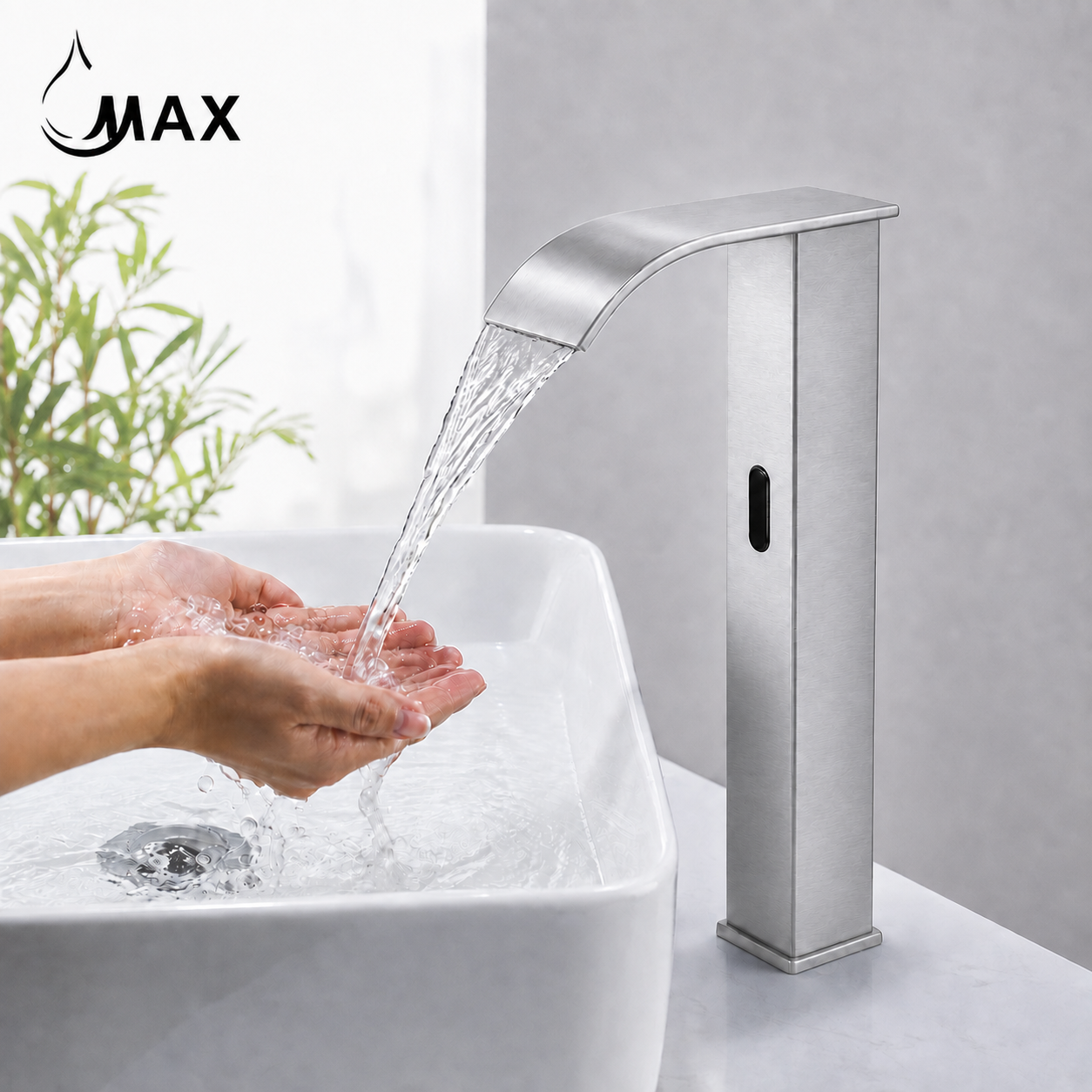 A modern brushed stainless steel waterfall bathroom faucet shown installed beside a white sink, with water flowing into a person's hands. A small 'MAX' logo appears in the upper left corner.