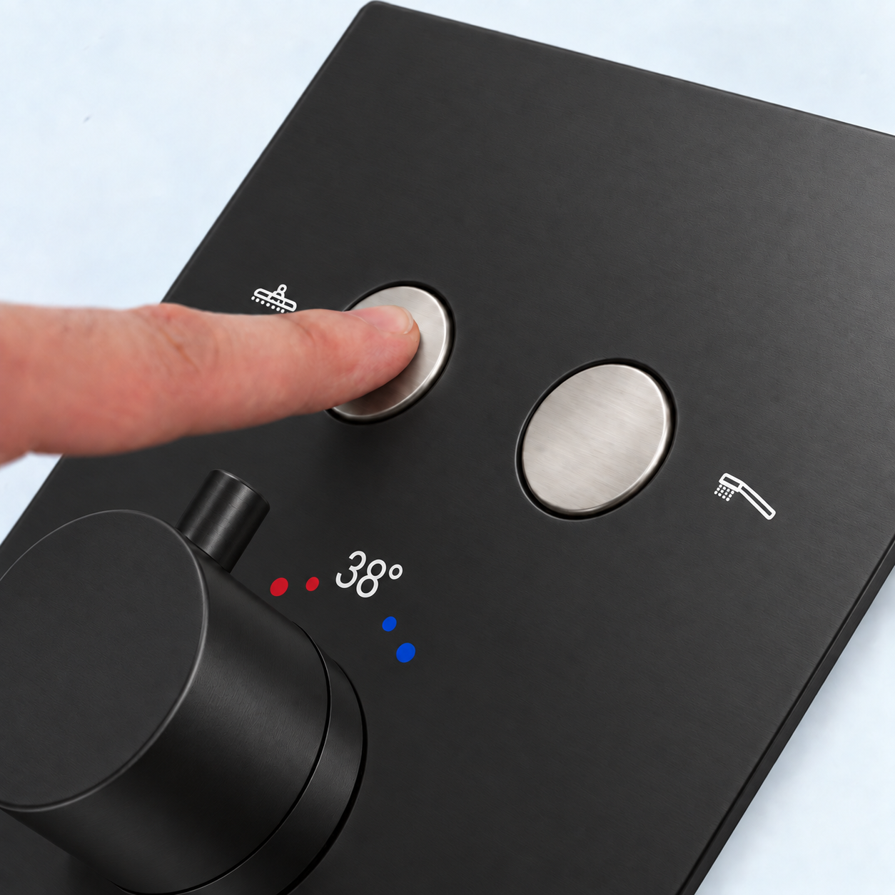 Close-up of a matte black shower valve trim with a finger pressing a round silver button, showing white icon symbols and a 38-degree temperature display.