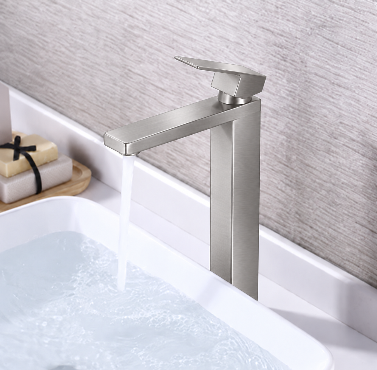 A modern single-handle bathroom faucet in brushed silver metal, shown with water running into a white sink against a textured gray wall.
