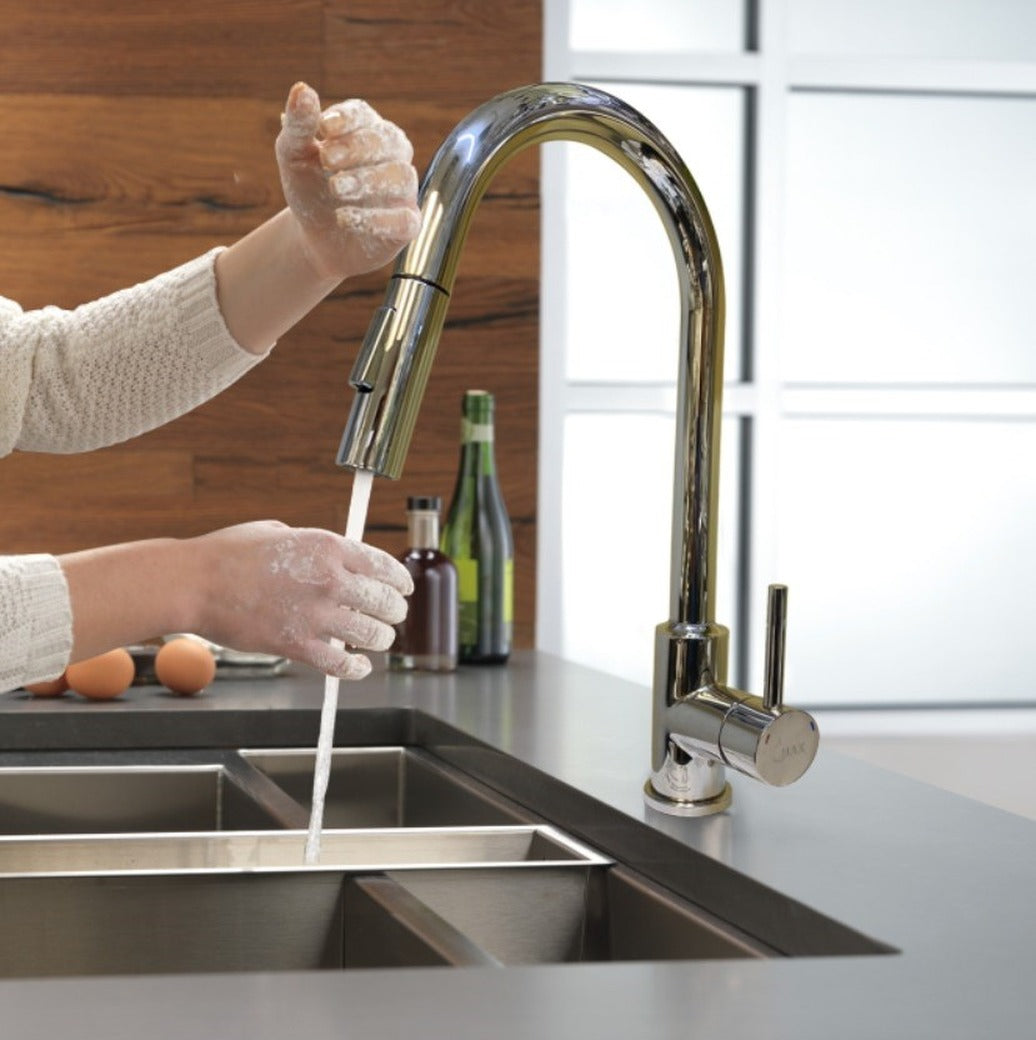 A person's hands using a chrome finish smart kitchen faucet with a pull-out spray nozzle over a sink.